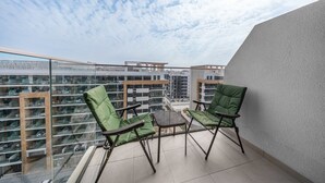 Un balcón con dos sillas verdes y una mesita, con vistas a un paisaje urbano con varios edificios.