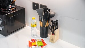 Una encimera de cocina con un microondas, una botella de agua, un plato con sobres de café, un juego de utensilios de cocina y un bloque de cuchillos.