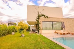 A modern house with a swimming pool, a patio with lounge chairs, and a well-maintained garden.