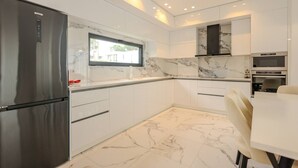 Una cuina moderna amb armaris blancs, un refrigerador d'acer inoxidable, un forn encastrat i una barra posterior de marbre.