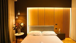 Et moderne hotelværelse med en stor seng, et natbord med en vase med blomster, og et sengebord med en lampe.