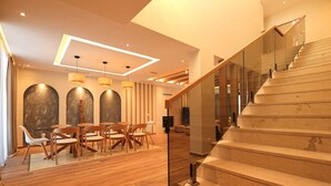 A modern interior with a wooden floor, a dining area with chairs and tables, and a staircase with glass railings. - SanPietro Elite Signature Villa (Plazhi San Pietro)