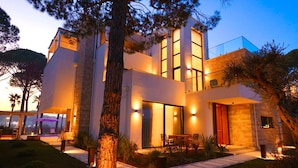 A modern two-story house with a patio, large windows, and a well-lit entrance. - SanPietro Elite Signature Villa (Plazhi San Pietro)