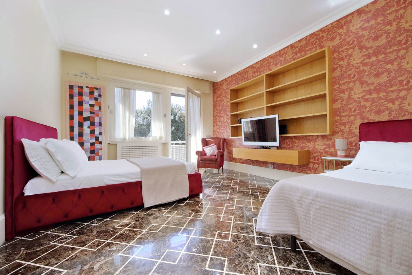 Habitació d'hotel amb dos llits, una televisió, un butacó vermell i un mur amb un disseny decoratiu.