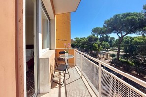 Ein Balkon mit Tisch und Stühlen, einem Blumentopf und Blick auf Bäume sowie einen Parkplatz.