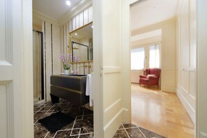 Een badkamer met een marmeren vloer, een zwart aanrichting, een spiegel, en een rode stoel in de aangrenzende kamer.