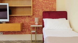 Ein Hotelzimmer mit Bett, Fernseher auf einer Holztruhe und einem kleinen Tisch mit Lampe.