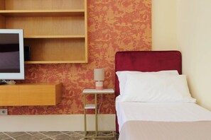 Ein Hotelzimmer mit Bett, Fernseher auf einer Holztruhe und einem kleinen Tisch mit Lampe.