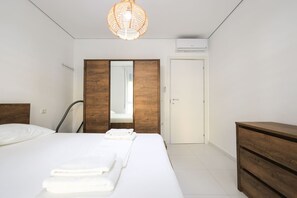 A modern bedroom with a bed, a wooden wardrobe, a mirror, and a hanging light fixture. - Cozy Getaway near the Beach (Plazhi San Pietro)
