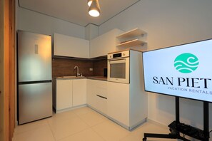 Eine moderne Küche mit weißen Schränken, einem Edelstahl-Kühlschrank und einem Backofen. Ein Flachbildfernseher zeigt das Logo von San Pieti Vacation Rentals.