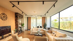 Een moderne woonkamer met een grote flatscreen-tv, comfortabele banken, een salontafel en een groot raam met uitzicht op de omgeving.