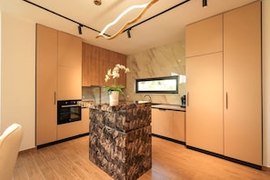 Una cocina moderna con una isla de mármol, armarios de madera y una orquídea en maceta.