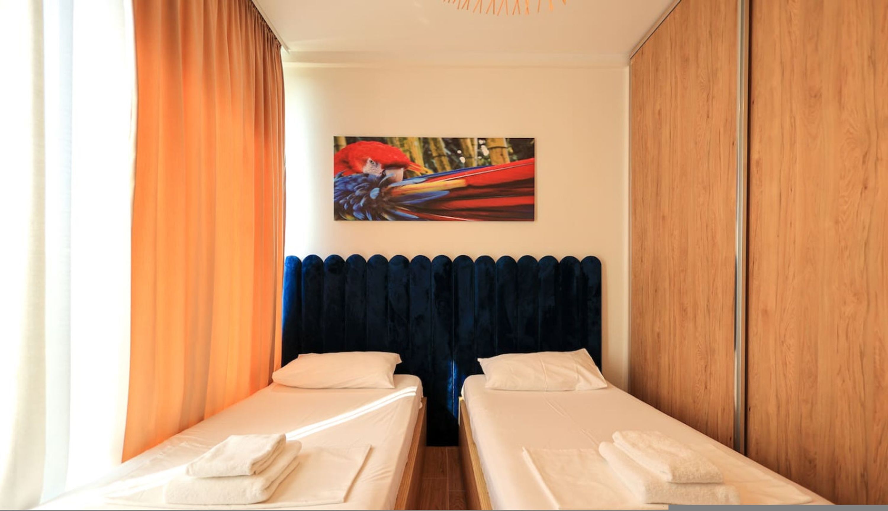 Habitación de hotel con dos camas, un cuadro grande de un loro y un armario de madera.