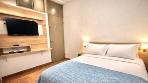Ein Hotelzimmer mit einem Bett, einem wandmontierten Flachbildfernseher, einem Kleiderschrank und einem Nachttisch mit Lampe.