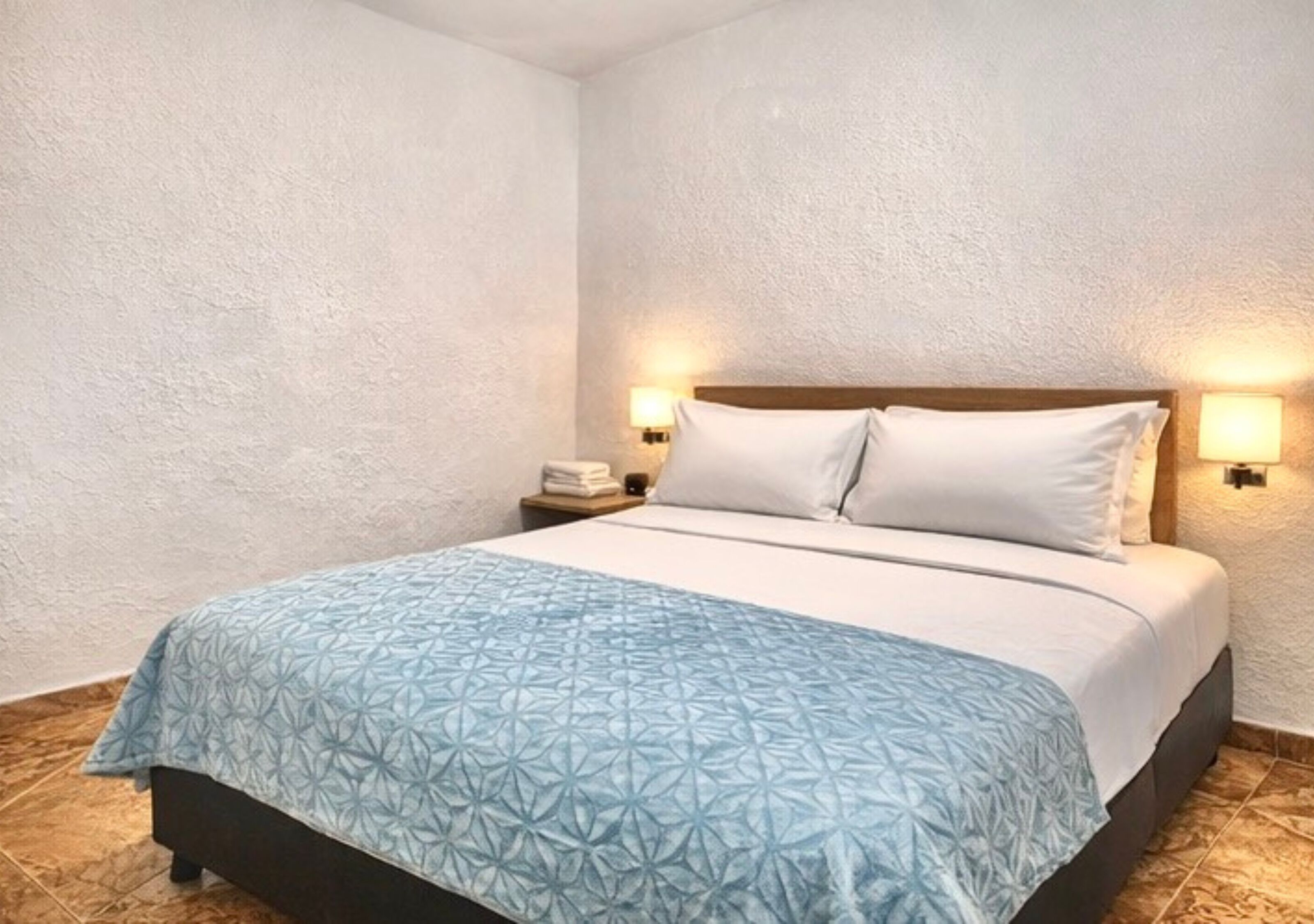 A bedroom with a bed, two bedside lamps, a nightstand, and a textured wall.
