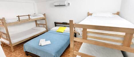 Un dormitorio con literas, una colcha azul, una almohada amarilla y un equipo de aire acondicionado en la pared.