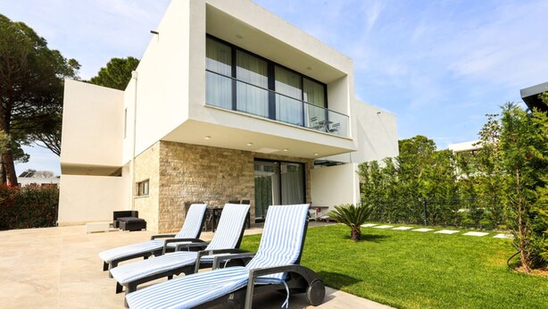 Ein modernes, zweistöckiges Haus mit Balkon, einem gepflegten Rasen und Liegestühlen.