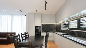 Eine moderne Küche mit Essbereich, ausgestattet mit einer Marmorarbeitsplatte, Einbaugeräten und einem schwarzen Esstisch mit Stühlen.