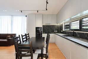 Une cuisine moderne avec un coin repas, dotée d’un pare-feu en marbre, de meubles blancs et d’un plan de travail noir.