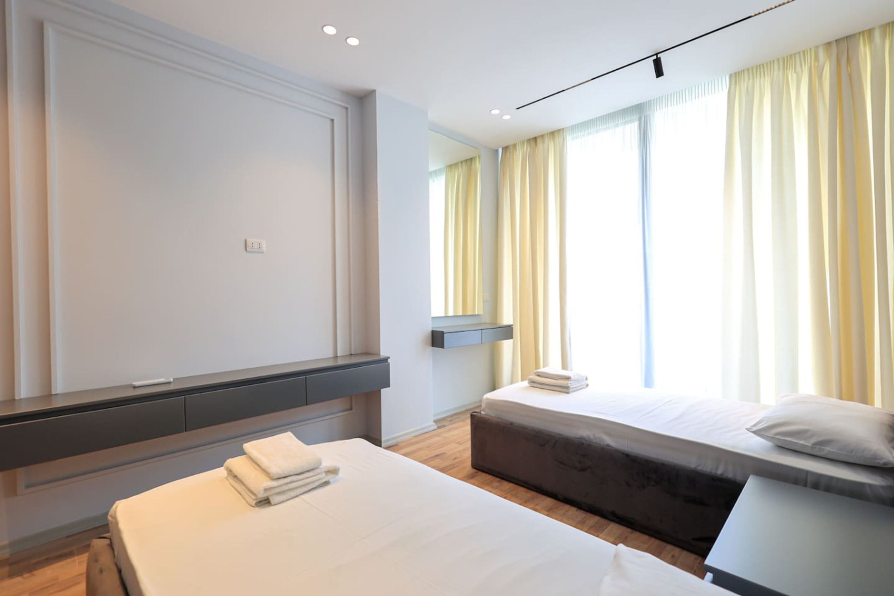 Habitación de hotel moderna con una cama grande, otra más pequeña, un escritorio y un espejo.