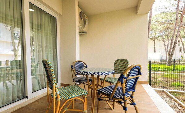 En balkon med et bord og stole, en skydedør samt udsigt til en have med hegn.