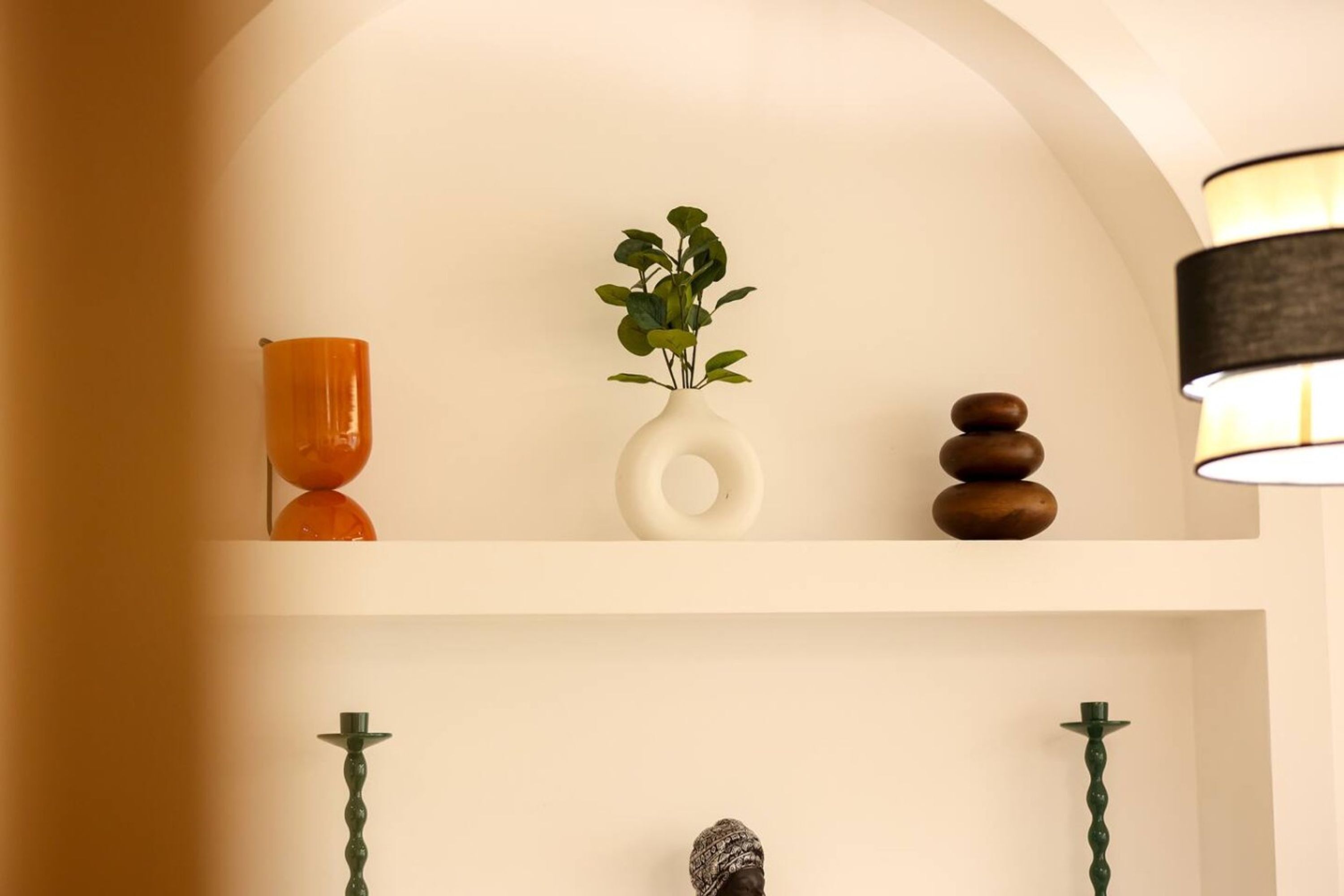 Una estantería con un jarrón blanco, una planta, un candelabro y una pila de objetos de madera.