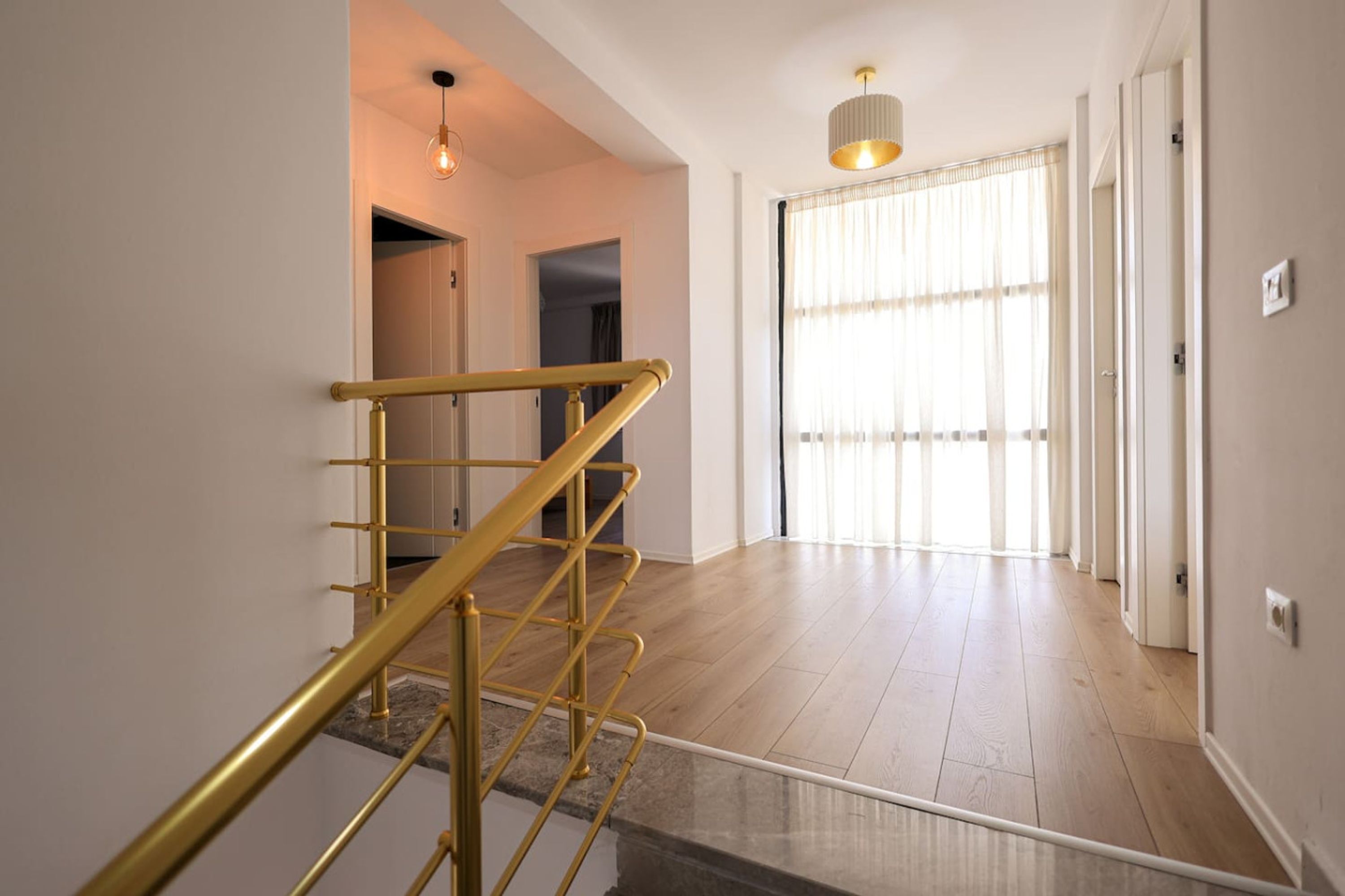 A staircase with a golden handrail leading to a room with a large window and a light fixture above.