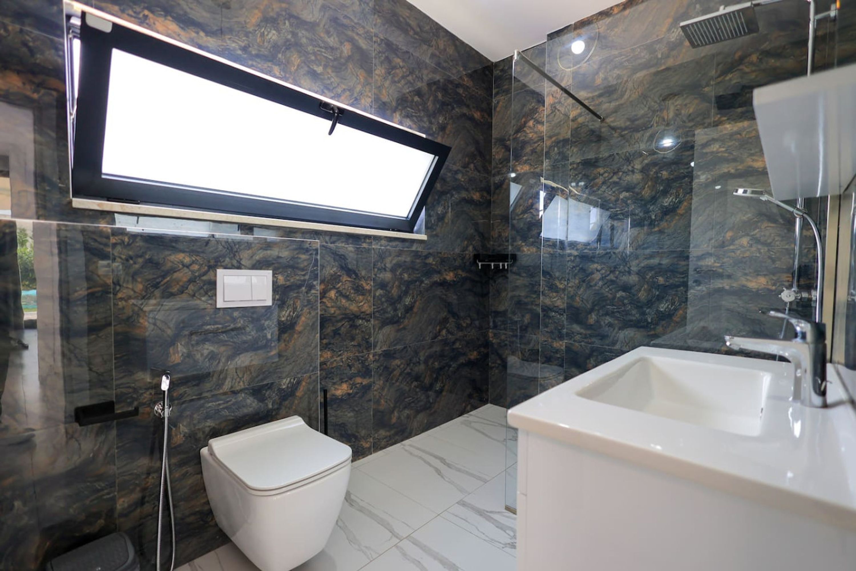 Ein modernes Badezimmer mit Marmorwand, Toilette, Dusche und Waschbecken.
