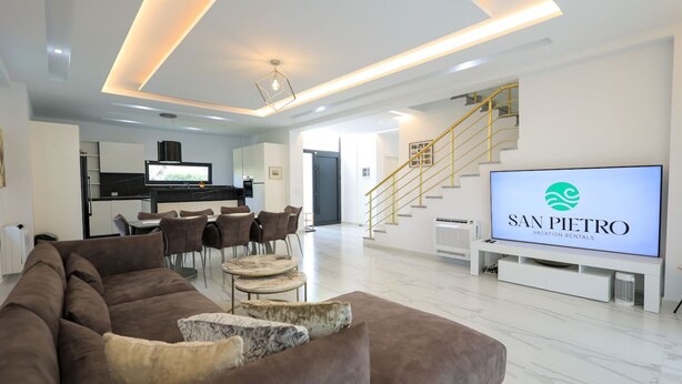Un moderno salón con un televisor de pantalla plana grande que muestra 'SAN PIETRO Vacation Rentals'.