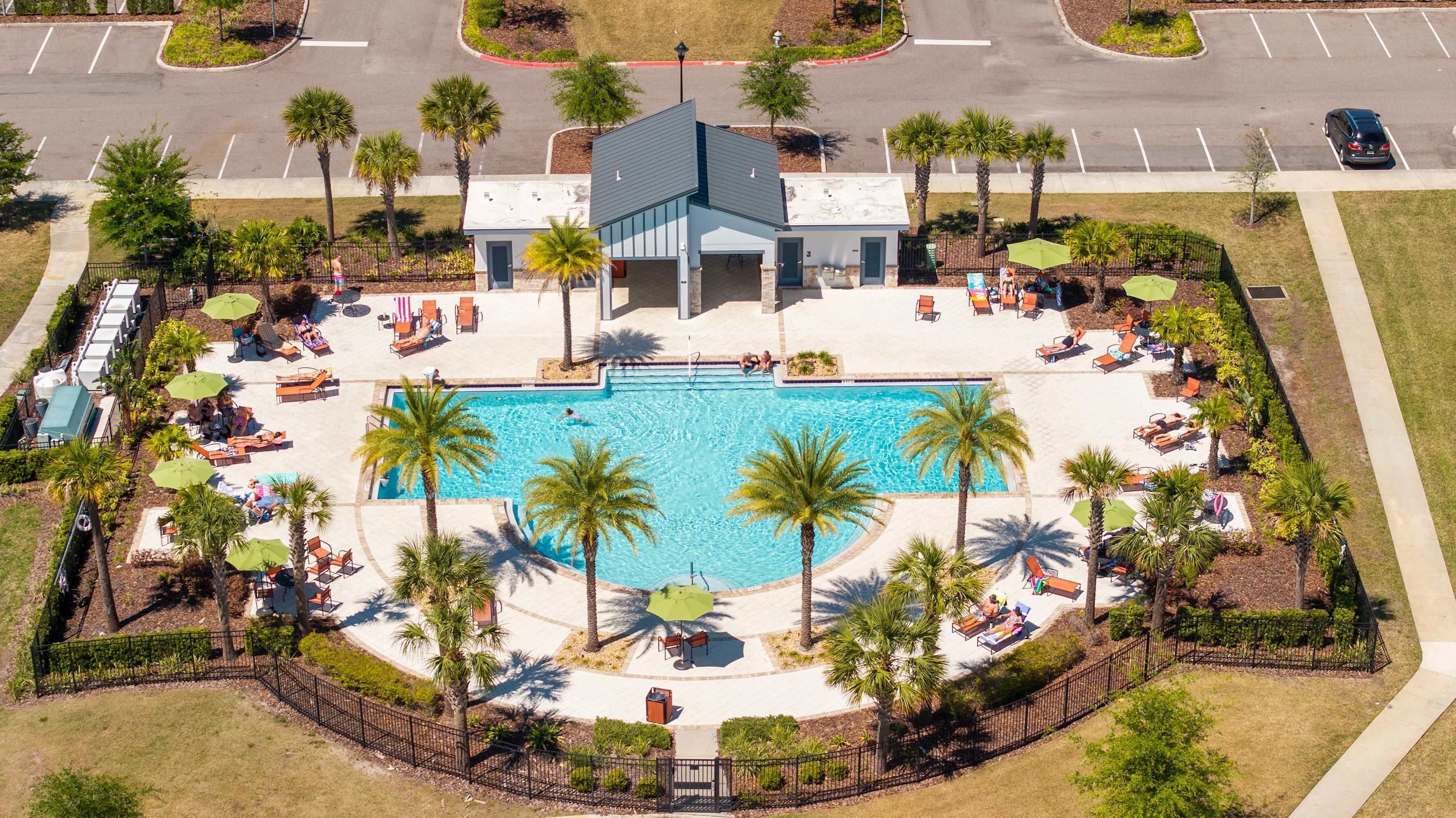 An aerial view of a resort with a central swimming pool surrounded by palm trees and lounge chairs.