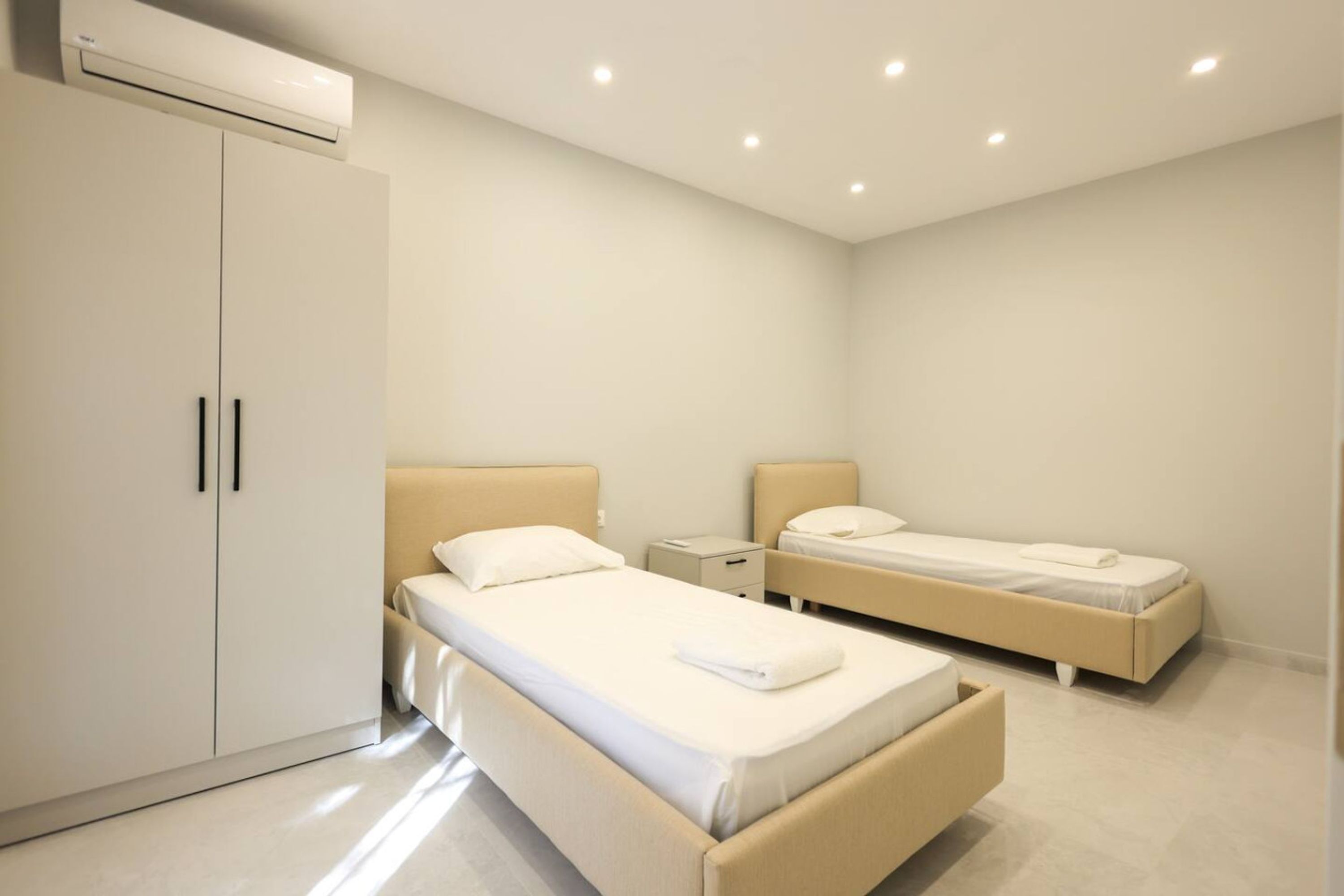 Et moderne hotelværelse med to senge, et garderobeskab, et natbord og en aircondition.