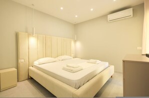 A modern bedroom with a large bed, bedside tables, an air conditioning unit, and a small cabinet. - Lura Apartment 001 in Durrës (Durrës)