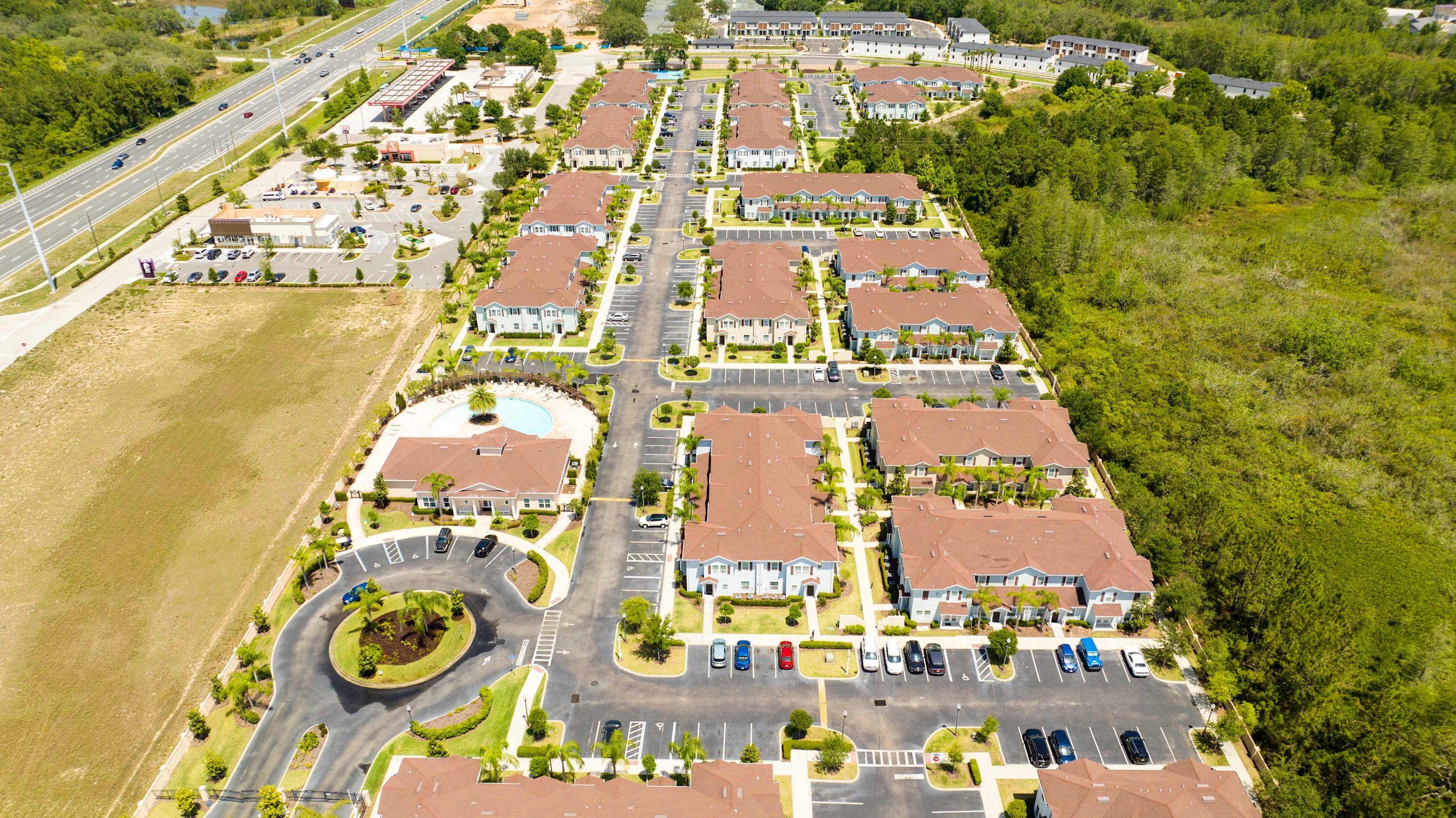 Luchtbeeld van een woonwijk met meerdere twee-onder-een-vlakhuiswoningen, een centrale rotonde en een parkeerplaats.