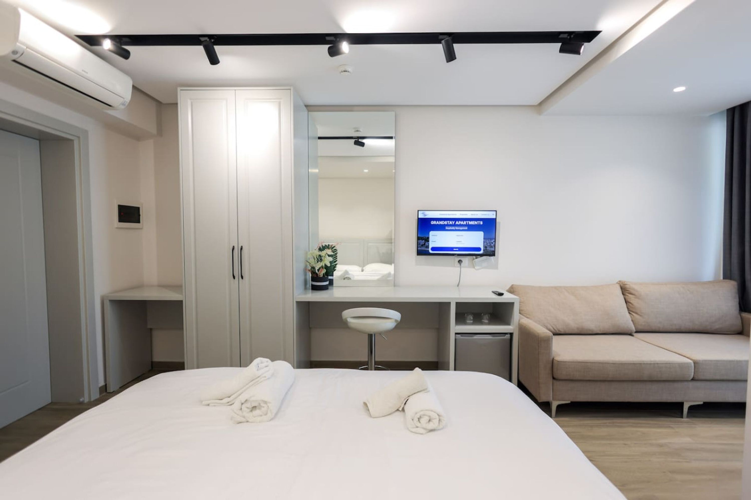 Una habitación de hotel moderna con cama, escritorio, sofá, televisor y armario.
