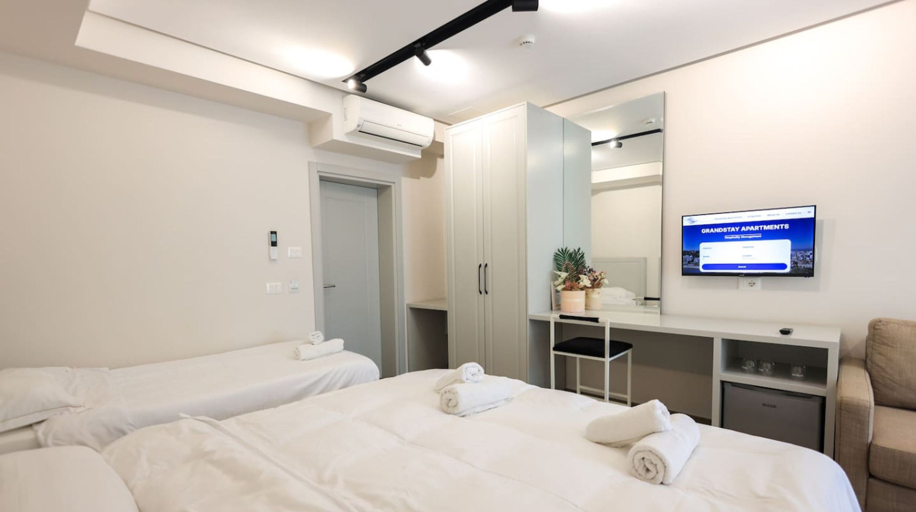 Ein Hotelzimmer mit zwei Betten, einem Schreibtisch, einem Stuhl, einem Fernseher und einem Kleiderschrank.