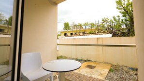 A balcony with a white chair and table, a view of a building, and a tree. - Beach Room 02 in Durrës (Durrës)