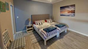 Un dormitorio con cama, mesita de noche, silla, alfombra, ventilador de techo y un cuadro en la pared.