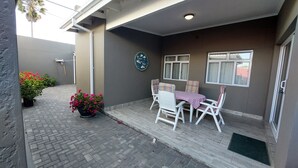 Un patio techado con mesa y sillas, plantas en macetas y un letrero colgado en la pared.