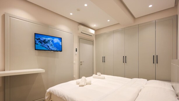 A modern bedroom with a large bed, a mounted TV, and built-in wardrobes. - Beach Apartment 01 in Durrës (Durrës)