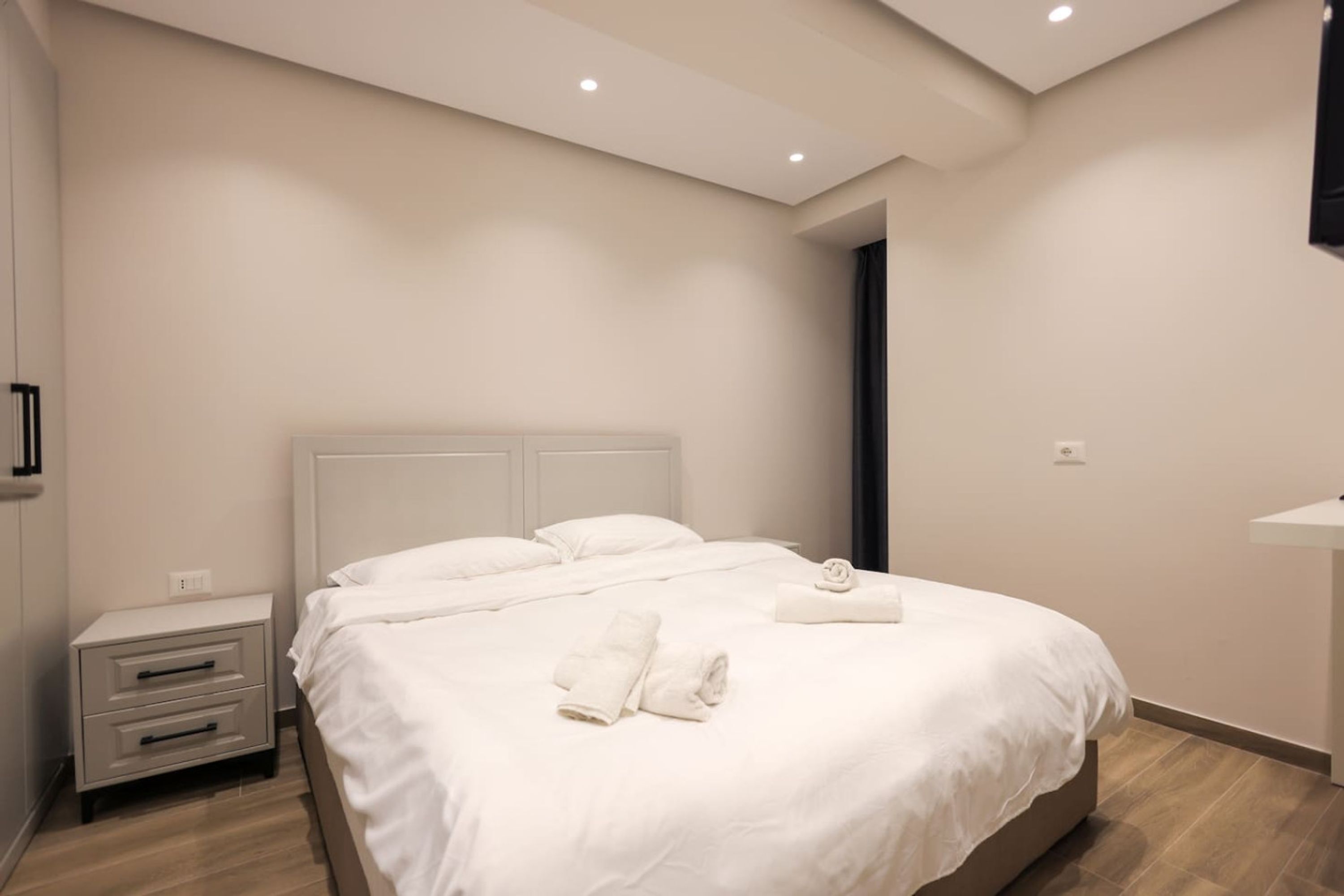 A modern hotel room with a large bed, a nightstand, a bedside table, and a built-in TV.