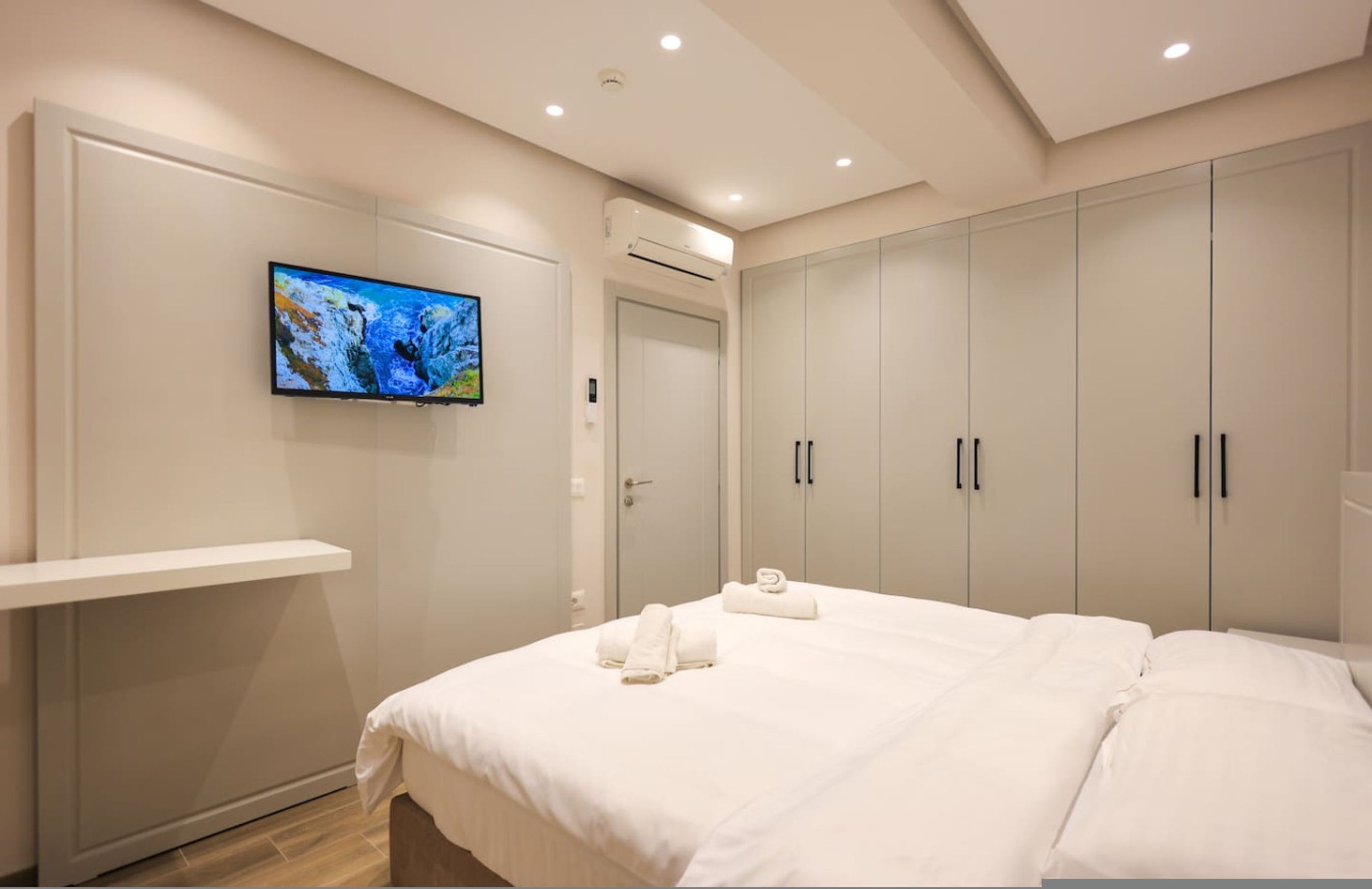 Ein modernes Schlafzimmer mit einem Bett, einem an der Wand montierten Fernseher und einem Kleiderschrank.