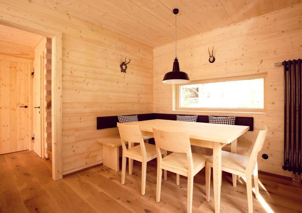 Un intérieur en bois comprenant une table à manger, des chaises, un banc, une lampe suspendue et une fenêtre.