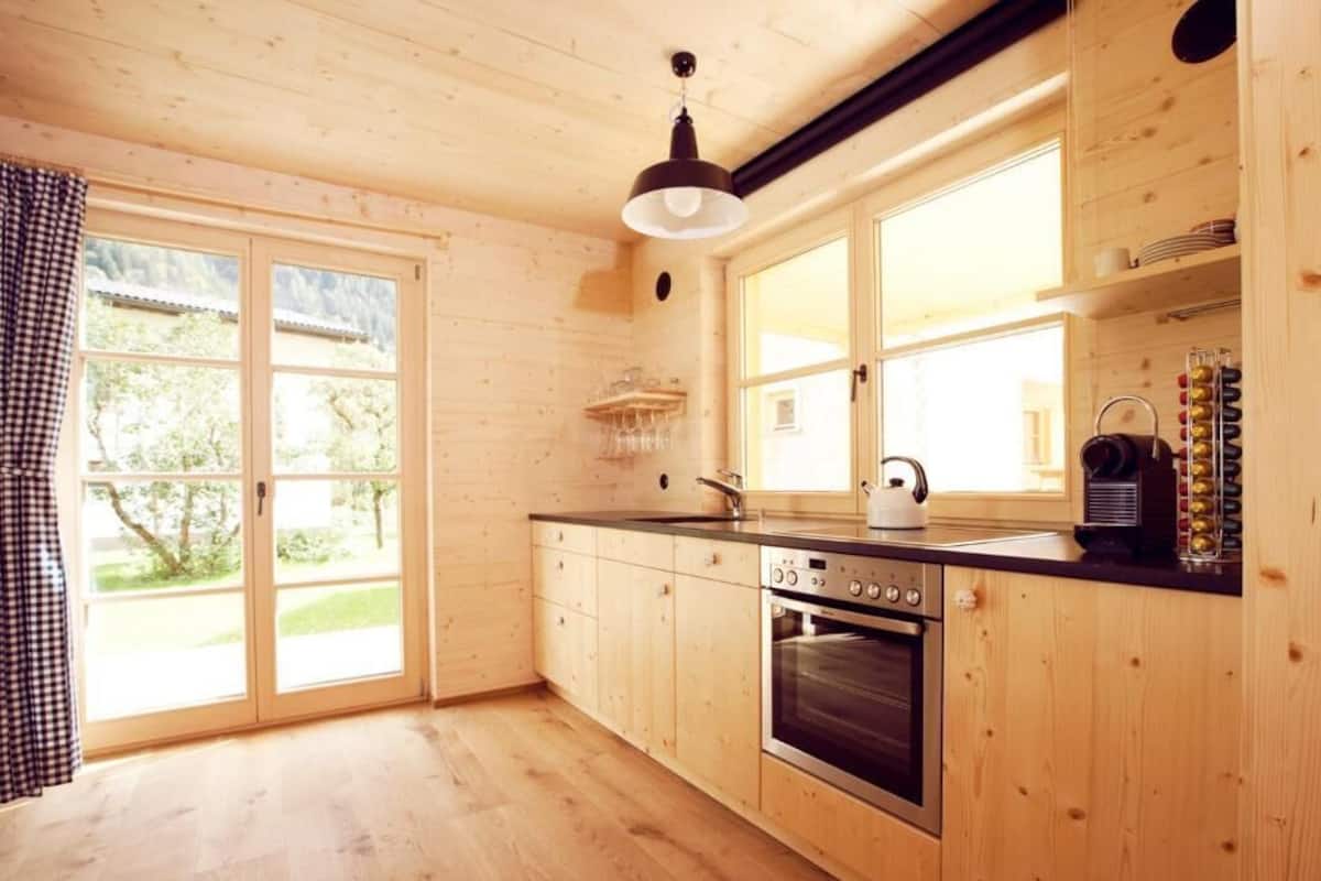 A wooden interior with a kitchen, including a stove, sink, and large windows.