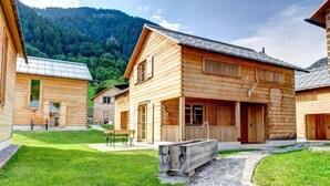 A wooden cabin with a stone pathway, a bench, and a table in the yard. - CASALPIN Chalets (Brand)