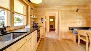A wooden cabin interior with a kitchen, dining area, and a hallway leading to a bedroom. - CASALPIN Chalets (Brand)