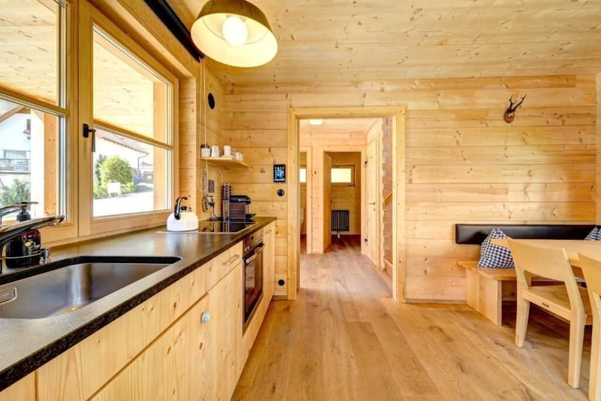 A wooden cabin interior with a kitchen, dining area, and a hallway leading to a bedroom.
