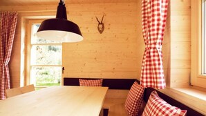 A wooden cabin interior with a wooden table, checkered curtains, a mounted animal skull, and a bench with pillows. - CASALPIN Chalets (Brand)
