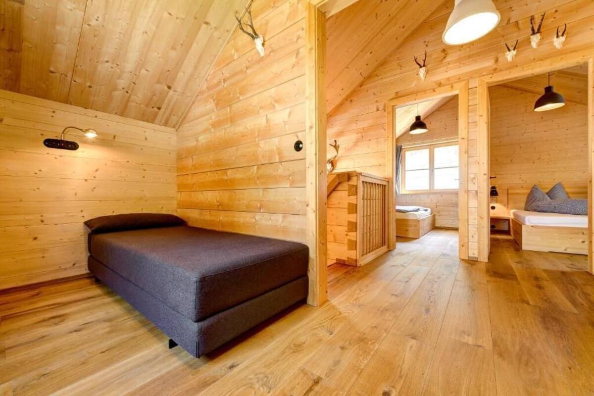 A log cabin interior with a bed, a small seating area, and a window.