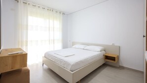 A minimalist bedroom with a bed, bedside tables, and a window with sheer curtains. - SanPietro Vacation Apartment 042 (Plazhi San Pietro)