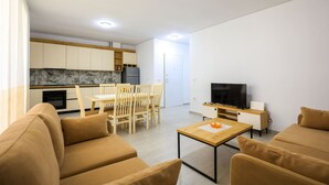 A modern living room with a sofa set, a dining table with chairs, a TV, and a kitchen area with cabinets and a marble backsplash. - SanPietro Vacation Apartment 042 (Plazhi San Pietro)